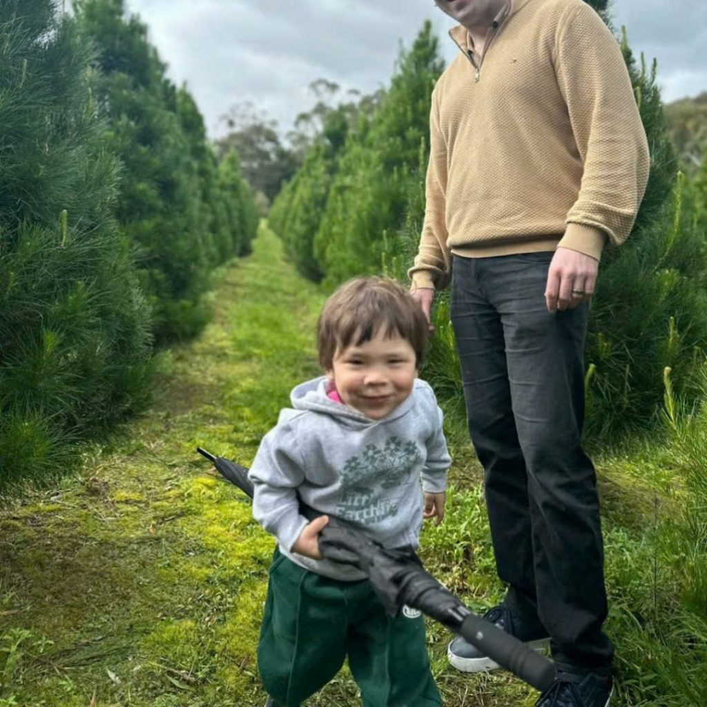 a man and child standing in a field of real christmas trees